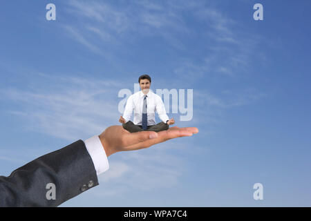 Geschäftsmann sitzt auf menschlicher Hand und macht Yoga-Pose Stockfoto