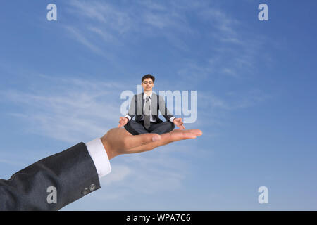 Geschäftsmann sitzt auf menschlicher Hand und macht Yoga-Pose Stockfoto