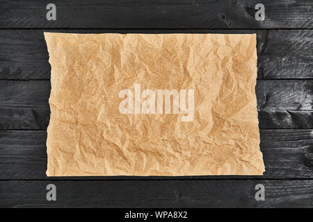 Zerknitterte Stück Pergament- oder Backpapier auf schwarzer Holztisch. Ansicht von oben. Kopieren Sie Platz für Text und Design Element. Stockfoto