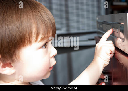 Kaukasier Kind, 3-4 Jahre alt aus der Nähe von Boy's Gesicht nah an DVD-Player vor ihm Suchen, und drücken Sie die Taste Play, um mit einem Finger. Stockfoto