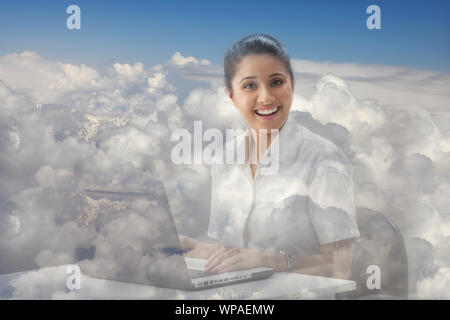 Geschäftsfrau sitzt auf Wolken und arbeitet auf einem Laptop Stockfoto