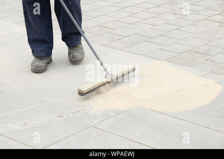 Bürgersteig Bauarbeiter Füllen der Fugen mit Sand mit einem langen Besen, schlichten Straße pflastern Stockfoto