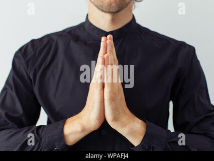 Junger bärtiger Mann trägt schwarzes Hemd mit Händen in betenden Pose isoliert auf weißem Hintergrund. Konzept der Religion oder Yoga. Stockfoto