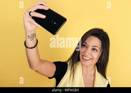 Portrait von fröhliche junge Frau lächelnd und unter selfie in Gelb Hintergrund isoliert Stockfoto