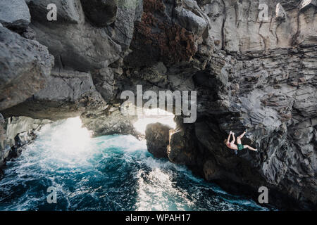 Man Klettern über dem Ozean in einem vulkanischen Höhle Stockfoto