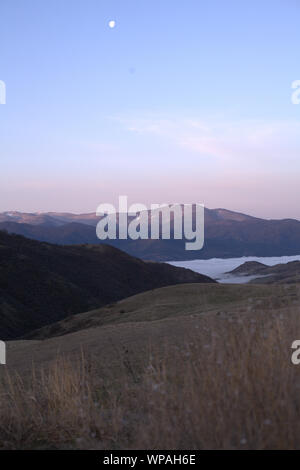 Ashland Snowy Mountains und den nebligen Tal im Sonnenaufgang morgen Licht, mit blauem Himmel und weissen Mond und trockene Blumen im Hintergrund Stockfoto