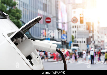 EV Automotive, Luftverschmutzung und Treibhausgasemissionen Konzept reduzieren. Laden Elektroauto mit blur Stadtblick Hintergrund. Stockfoto