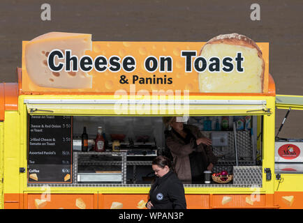 Junge Frau zu Fuß vorbei an einem Mobile food Konzession verkaufen Käse auf Toast. Strand in Southport, Merseyside, UK Stockfoto