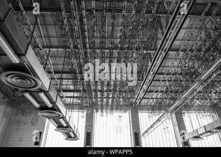 BW Ton, Low Angle Innenansicht der offenen Decke der alten Fabrik aufgeben oder industrielle Gebäude, AC verhalten System und hängenden Ketten zeigen. Stockfoto