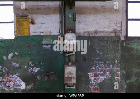 Stromzähler, Leistungsschalter und Kabel system auf rauen alten Kratzer mit weißen und grünen Mauer in verlassen industriellen Gebäude bemalt. Stockfoto