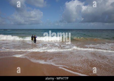 Ein Schwimmer und Paddel boarder stehen am Rand des Meeres in Grève de Lecq, St Ouen, Jersey, Channel Islands. Stockfoto