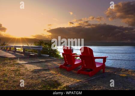 Zwei einsame rote Stühle auf der kanadischen Ostküste während des Sonnenuntergangs. Stockfoto