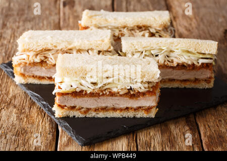 Hausgemachte Sandwiches mit Schweinekotelett, Sauce und frischen Kohl close-up auf einer Schiefertafel Board auf einem Holztisch. Horizontale Stockfoto