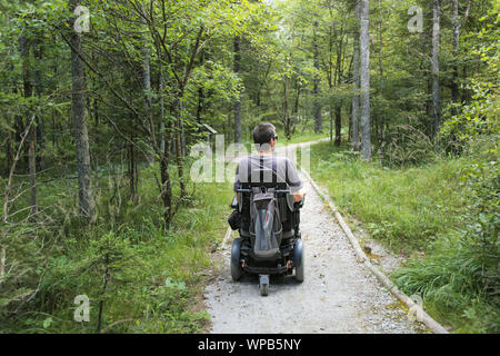 Glückliche Menschen im Rollstuhl in der Natur. Erkunden Wald Wildnis auf eine zugängliche Schmutz weg. Stockfoto