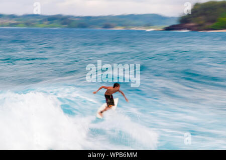 Junger Mann, der auf einem Surfbrett in eine blaue Welle im Sommer. Stockfoto
