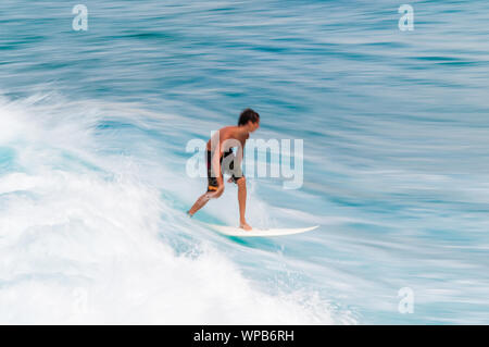 Junger Mann, der auf einem Surfbrett in eine blaue Welle im Sommer. Stockfoto