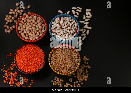 Rote und braune Linsen, Kichererbsen und weißen Bohnen sind Hülsenfrüchte, viel Protein enthalten, sind auf einem dunklen Hintergrund in Schalen entfernt, horizontal Stockfoto