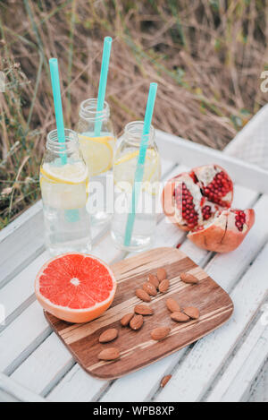 Picknick Set mit Grapefruit, Granatapfel, Mandel- Muttern und Limonade in Glasflaschen auf weißem Holz- Fach. Stockfoto