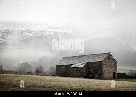 Schnee Sturm nähert sich eine Scheune in einem ländlichen Gebiet im Winter mit Kinder Scout im Hintergrund. Peak District, Derbyshire, England, Großbritannien Stockfoto