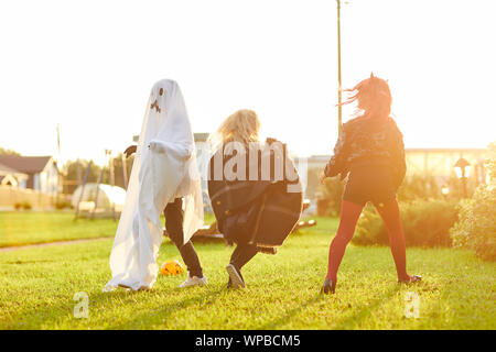 In voller Länge Porträt der glückliche Kinder tragen Kostüme, die auf grünen Rasen, während Spaß an Halloween und Spielen im Sonnenlicht, kopieren Raum Stockfoto