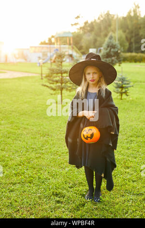 Volle Länge Portrait von cute Teenager verkleidet als Hexe posiert im Freien auf Halloween und Holding Trick oder Festlichkeit Korb, kopieren Raum Stockfoto