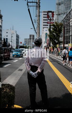 MATSUYAMA, Japan - 04.August 2019: Eine vertikale selektive Aufnahme eines männlichen Handschuhe und Mütze stehend in der Nähe einer Straße mit Autos und Gebäude Stockfoto