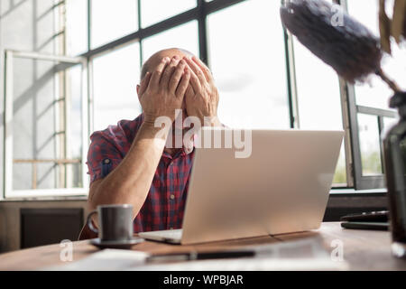 Senior kaukasischen Mann seine müden Augen reiben. Er ist müde auf dem Laptop Bildschirm zu sehen. Negativen Gesichts menschliche Emotion über Verlust von Geld. Stockfoto