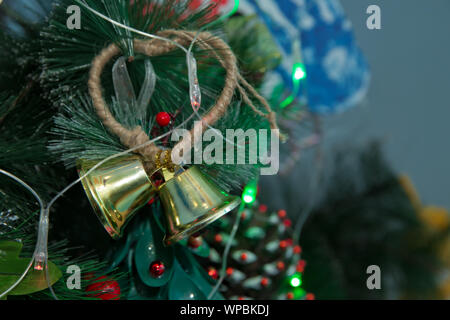 Weihnachten goldene Glocken mit Weihnachten Garnituren auf Pine Tree Hintergrund eingerichtet. Bell mit gelben Kugel vor Weihnachtsbaum. Neues Jahr Stockfoto