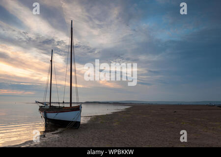 Ein Segelboot ist langsam durch die steigende Flut an instow Beach in North Devon, wie die Sonne umgeben. Stockfoto