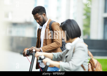 Seitenansicht Porträt zweier Menschen reiten Elektroroller in Stadt Straße, auf Afrikaner - der Mann im Hintergrund, kopieren Raum konzentrieren Stockfoto