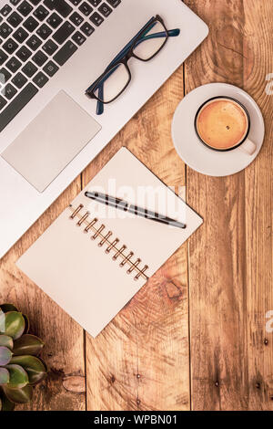 Senkrechte Draufsicht auf die Zusammensetzung der moderne Büro Arbeitsbereich mit Laptop, Notizbuch, Kaffee und Anlage auf einem rustikalen Holztisch. Office arbeiten, studieren Konzepte Stockfoto