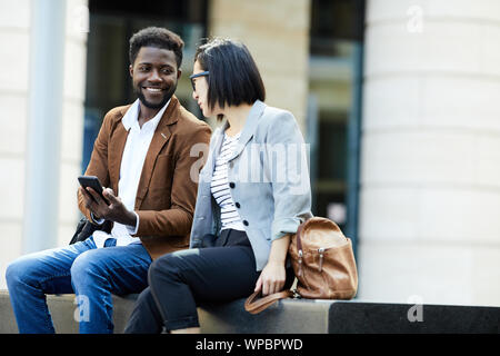 Porträt von zwei junge Geschäftsleute Entspannung im Freien während der Pause, afrikanischer Mann und die asiatische Frau fröhlich plaudernd, Kopie Raum