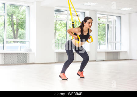 Portrait der junge Schöne passende Frau in Schwarz Sportswear training Arme mit trx fitness Bänder in der Turnhalle tun Push-ups Zug Oberkörper Brust sollte Stockfoto