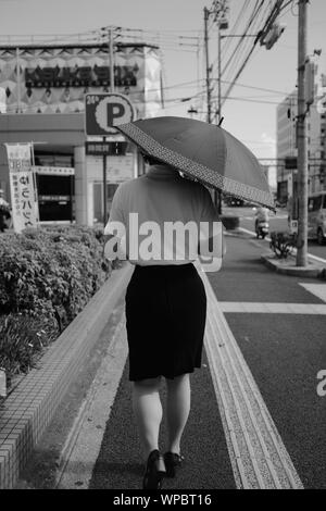 MATSUYAMA, JAPAN - May 30, 2019: ein Graustufen vertikale selektive Schoß einer Frau mit schwarzen Rock mit einem T-Shirt mit einem Regenschirm auf einem Sid Stockfoto