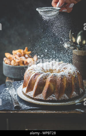 Landhausstil Apple Bundt Cake bestreut mit Puderzucker auf alten Holztisch mit Frau Hände Stockfoto