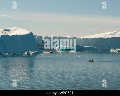 Eisberg und Eis vom Gletscher in den arktischen Natur Landschaft in Grönland. Antenne drone Foto von Eisbergen in Ilulissat Eisfjord. Durch den Klimawandel globale Erwärmung betroffen. Kleine touristische Boot. Stockfoto