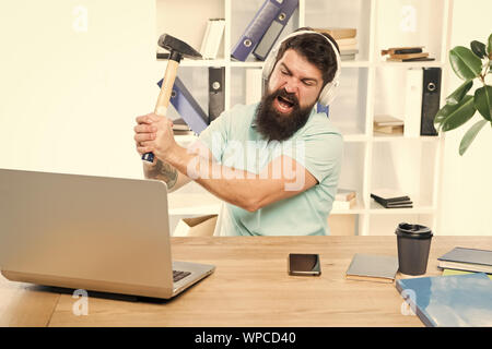 Veraltete Software. Computer lag. Gründe für Computer zurückbleiben. Wie fix langsam hinterher. Hasse office Routine. Man bärtige Kerl Kopfhörer Büro schwingen Hammer auf dem Computer. Langsame Internetverbindung. Stockfoto