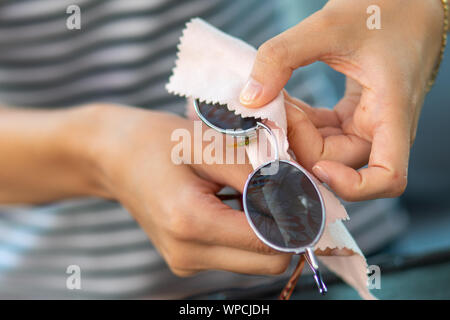 Frau Hände Reinigung Ihrer Sonnenbrille mit Mikrofasertuch wischen, wischen Sonnenbrille Stockfoto