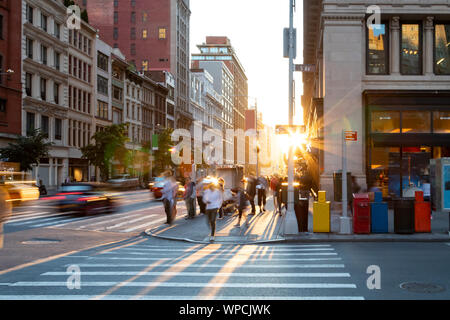 Mann zu Fuß durch die zebrastreifen an der belebten Kreuzung der 5th Avenue und der 23. Straße in New York City mit hellen Licht des Sonnenuntergangs in der backgroun Stockfoto