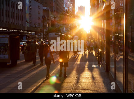 NEW YORK CITY 2019: Menschenmassen werfen lange Schatten, als Sie in das helle Licht des Sonnenuntergangs auf die 34th Street in Manhattan NYC. Stockfoto