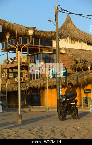 MANCORA, PERU - 20. AUGUST 2013: Unbekannter junger Mann auf dem Motorrad beobachten, die untergehende Sonne und Strand am 20. August 2013 in Mancora, Peru. Stockfoto