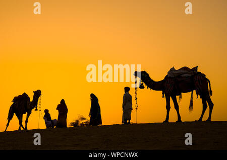 Jaisalmer, Rajasthan, Indien - 18. April 2018: Indische Kameltreiber (camel Drivers) mit Kamelen Silhouetten in Dünen der Wüste Thar auf den Sonnenuntergang. Stockfoto