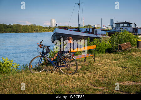 Wien, Österreich - 14 August 2019: ein Radfahrer ruht auf einer Bank neben der Donau. Stockfoto