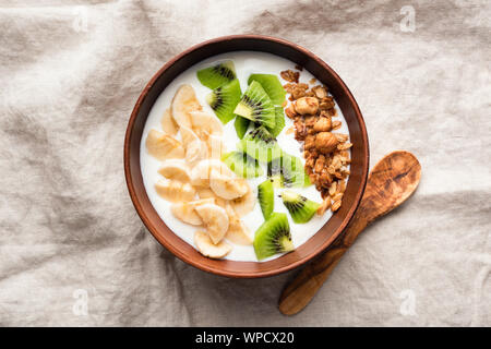 Joghurt Schale mit tropischen Früchten Kiwi, Banane und Haferflocken Müsli in der Schüssel, Ansicht von oben. Gesundes Essen, sauber essen Konzept Stockfoto