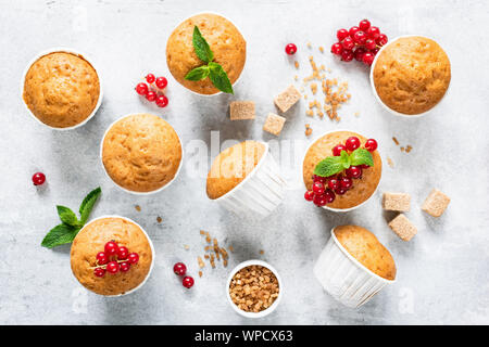 Vegan hausgemachte Muffins mit roten Beeren und Minze Blatt auf hellen Grau konkreten Hintergrund eingerichtet. Ansicht von oben. Hausgemachte leckere Muffins Stockfoto