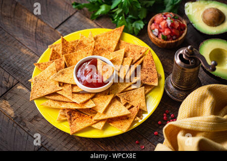 Mexikanische Tortilla Chips Nacho mit Tomatensauce und Salsa auf gelb Platte, Holz- Hintergrund. Tex Mex Essen Stockfoto
