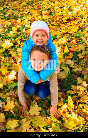 Junge hübsche Schwestern sitzen und auf gelben Blätter im Herbst Park umfassen. Kleine Kinder mit Blätter im Herbst. Kleine Mädchen im Herbst Wald. Herbstliche Stimmung. Ein Stockfoto