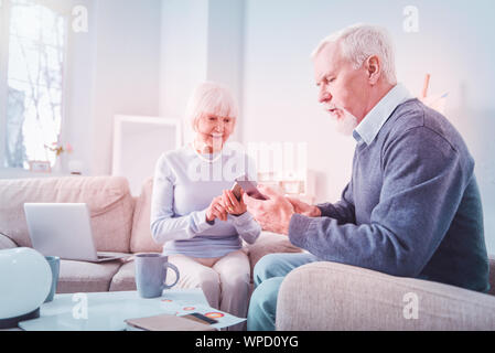 Moderne Rentner über ihre Smartphones auf dem Sofa zu Hause sitzen Stockfoto
