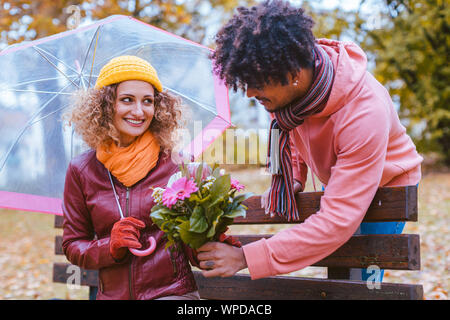 Mann überrascht seine Frau mit einem Strauß Blumen auf einem verregneten Herbst Tag Stockfoto