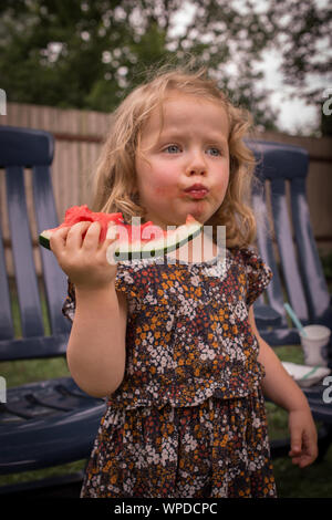 Adorable Vorschüler Mädchen mit lockigem Haar, saftig, lecker Essen, frische Wassermelone, lustiges Gesicht Stockfoto